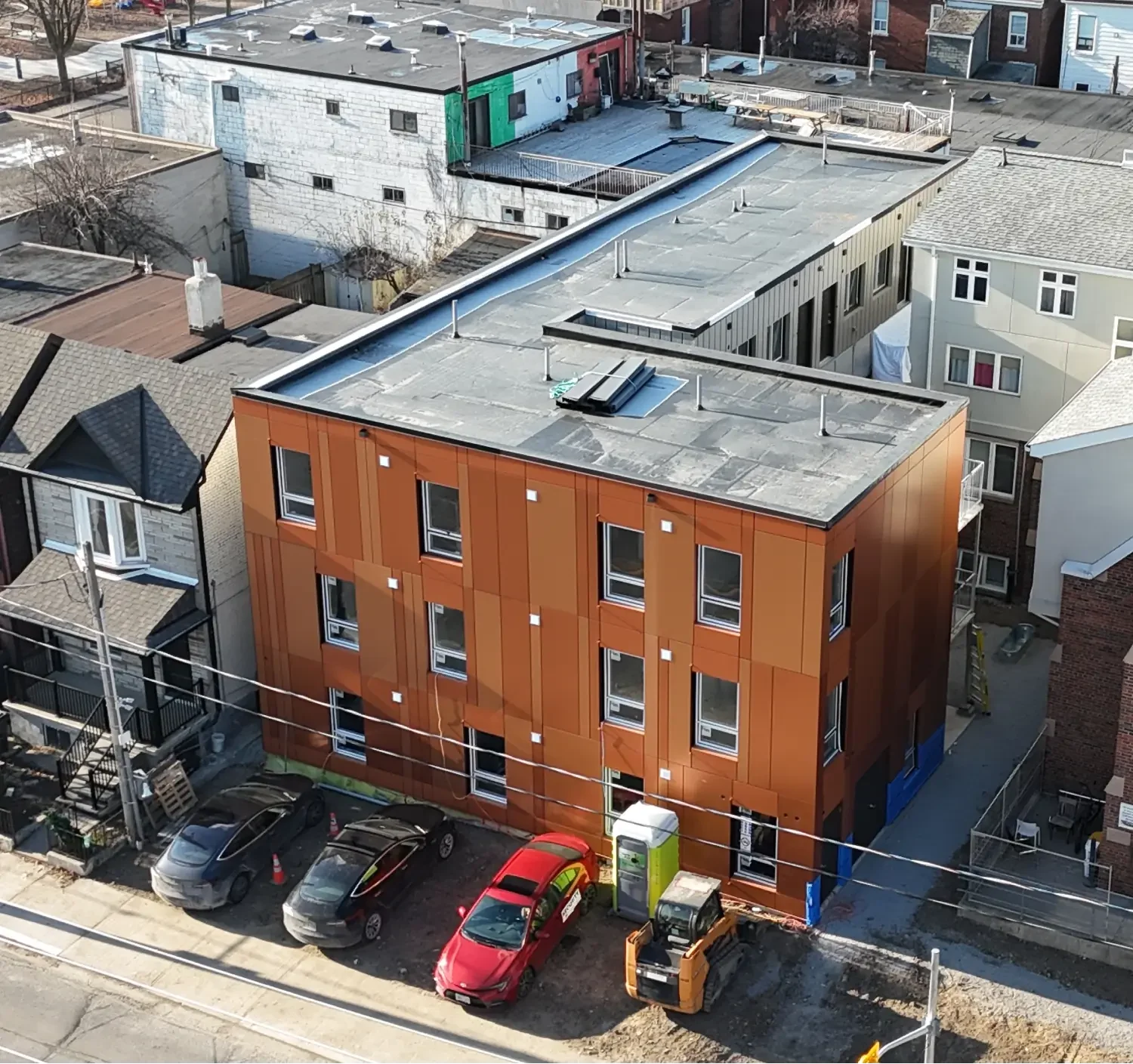 Street view of 1120 Ossington Ave, featuring a modern building with a brick facade next to a historic structure, surrounded by trees with autumn foliage